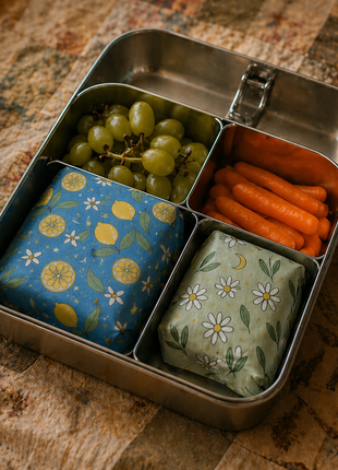Reusable beeswax wraps packed in a stainless steel lunchbox with grapes, carrots, and snacks for lunches and everyday use.