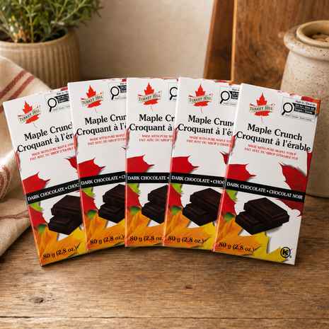 Five Maple Crunch dark chocolate bars made with pure maple syrup, fanned out on a rustic wooden kitchen table as a Canadian maple chocolate 5-pack.