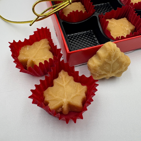 Close-up of soft maple sugar candies made from pure Canadian maple syrup, shaped like maple leaves in red paper cups, with a gift box in the background