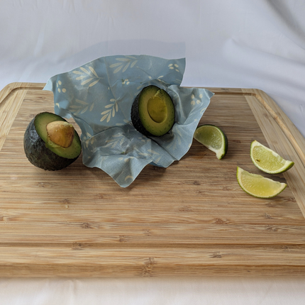 Beeswax food wrap keeping a cut avocado fresh on a bamboo cutting board with lime wedges