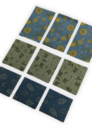 Complete 9-pack reusable beeswax food wraps made in Canada displayed with three retail packages and all nine wraps arranged by size in an angled product presentation on a white background.  Includes three large, three medium, and three small wraps made from cotton, Canadian beeswax, pine resin, and jojoba oil for eco-friendly, reusable food storage that helps reduce single-use plastic in the kitchen.