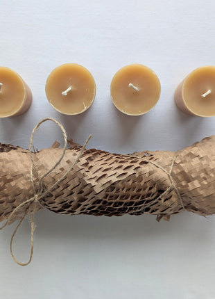 Top-down view of four beeswax votive refill candles displayed with their kraft honeycomb paper wrapping and natural twine.  The overhead angle clearly shows the candle tops, cotton wicks, warm beeswax colour, and rustic four-pack presentation.