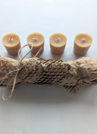 Four natural beeswax votive refill candles arranged above their kraft honeycomb paper wrapping and twine on a clean white background.  The image shows the full four-candle set, warm honey-gold wax colour, visible cotton wicks, and simple plastic-free presentation.