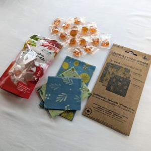 The Beeswax Wraps & Maple Candy Starter Set is arranged on a clean white background with a 3-pack of reusable beeswax food wraps, a 90 g bag of individually wrapped maple candies, loose candies, and all three folded wrap patterns.  This flat-lay image clearly shows the complete bundle and the products included.