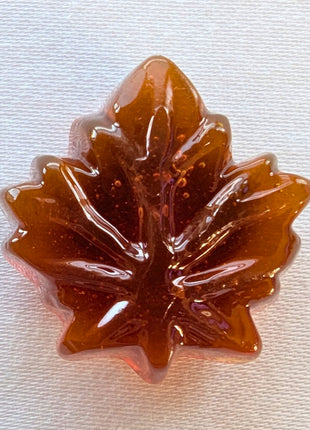 Close-up of an unwrapped Canadian hard maple candy showing its translucent amber colour and detailed maple-leaf shape. Made with pure maple syrup, this traditional Canadian maple sweet has the glossy appearance and moulded leaf design of a hard candy.