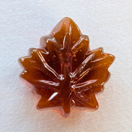 Close-up of an unwrapped Canadian hard maple candy showing its translucent amber colour and detailed maple-leaf shape. Made with pure maple syrup, this traditional Canadian maple sweet has the glossy appearance and moulded leaf design of a hard candy.