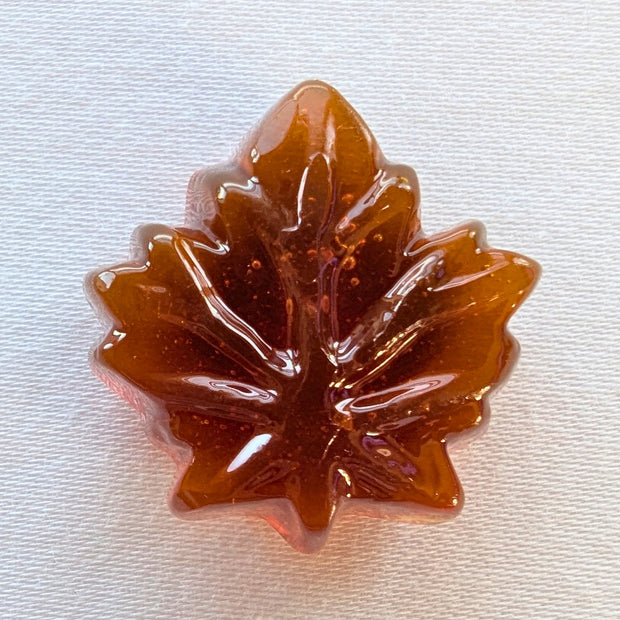 Close-up of an unwrapped Canadian hard maple candy showing its translucent amber colour and detailed maple-leaf shape. Made with pure maple syrup, this traditional Canadian maple sweet has the glossy appearance and moulded leaf design of a hard candy.