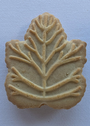 Close-up of an individual Canadian maple cream cookie showing its maple-leaf shape, embossed leaf pattern and golden baked surface. These Canadian sandwich cookies are made with pure maple syrup and feature a decorative maple leaf design associated with traditional Canadian maple treats.