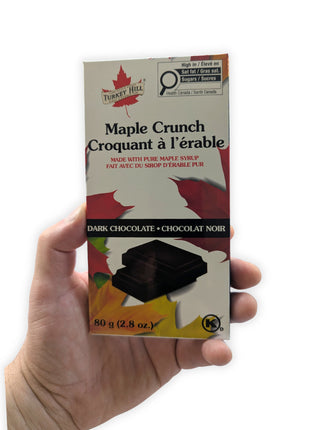 Canadian dark chocolate maple crunch bar held in one hand to demonstrate the size of the 80 g package.  This image shows the actual scale of the made-in-Canada maple chocolate bar, helping customers visualize its dimensions before purchase.