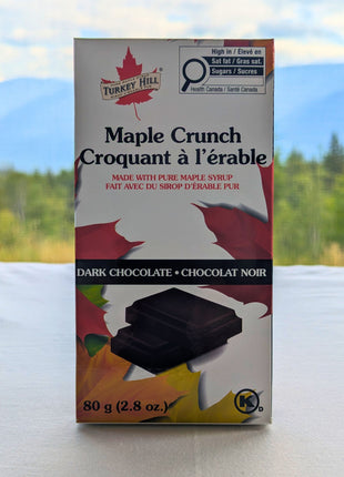 Canadian Maple Crunch dark chocolate bar displayed with a Canadian forest landscape in the background.  Canadian Maple Crunch Dark Chocolate Bar photographed against a scenic Canadian landscape, emphasizing its Canadian origin and maple heritage.