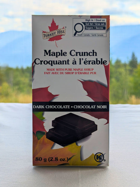 Canadian Maple Crunch dark chocolate bar displayed with a Canadian forest landscape in the background.  Canadian Maple Crunch Dark Chocolate Bar photographed against a scenic Canadian landscape, emphasizing its Canadian origin and maple heritage.