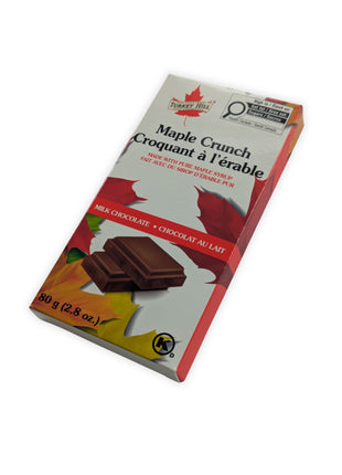 Angled view of Canadian Maple Crunch milk chocolate bar made with pure Canadian maple syrup in retail packaging.  The angled perspective provides a better view of the package depth and presentation while emphasizing its gift-ready appearance.
