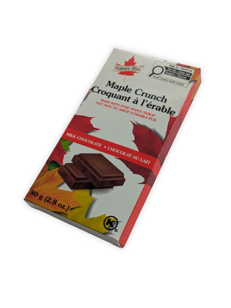 Angled view of Canadian Maple Crunch milk chocolate bar made with pure Canadian maple syrup in retail packaging.  The angled perspective provides a better view of the package depth and presentation while emphasizing its gift-ready appearance.