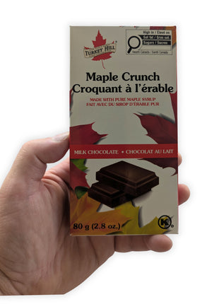Canadian milk chocolate maple crunch bar held in one hand to demonstrate the size of the 80 g package.  This image shows the actual scale of the made-in-Canada maple chocolate bar, helping customers visualize its dimensions before purchase.