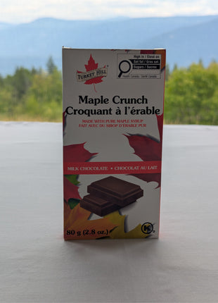 Canadian Maple Crunch milk chocolate bar made with pure Canadian maple syrup displayed outdoors against a scenic Canadian mountain landscape.  The natural mountain backdrop reflects the Canadian heritage and premium presentation of this maple-inspired chocolate gift.