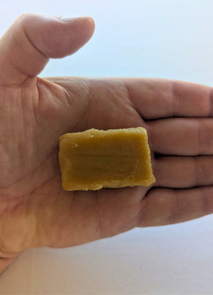 Hand-held view of a Canadian maple fudge candy showing the individual piece’s size, golden maple colour, and soft, slightly crumbly texture against an open palm.  Made with pure maple syrup, this close-up provides a natural sense of scale for the traditional Canadian maple confection while highlighting its handmade-style appearance and creamy fudge texture.