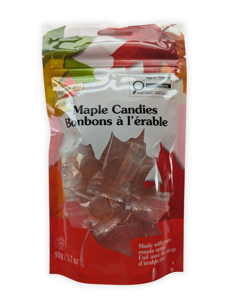 A front view of a 90 g resealable package of maple hard candies made with pure maple syrup, photographed on a clean white background.  The bilingual Maple Candies and Bonbons à l’érable label is clearly visible, along with the red maple-leaf packaging and individually wrapped amber maple-leaf candies shown through the transparent window.