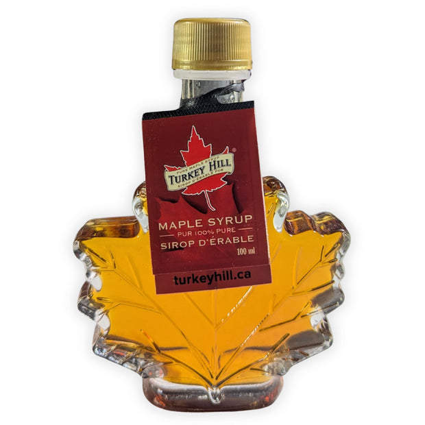 Front view of a 100 ml pure Canadian maple syrup maple leaf bottle with original supplier hang tag attached.  Authentic Canadian maple syrup presented in a classic glass leaf bottle, highlighting premium quality and traditional Canadian maple syrup packaging.