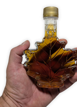 Pure Canadian maple syrup in a maple leaf glass bottle shown in hand to demonstrate the bottle size and shape.  Authentic maple syrup made in Canada with a classic souvenir bottle that makes an excellent Canadian gift or gourmet pantry staple.