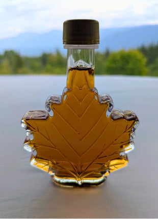 Pure Canadian maple syrup in a traditional maple leaf bottle displayed against a scenic Canadian mountain landscape.  Authentic maple syrup made in Canada, inspired by Canada's natural beauty and perfect for gifting, breakfast, baking, and enjoying genuine Canadian maple flavour.