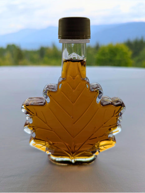Pure Canadian maple syrup in a traditional maple leaf bottle displayed against a scenic Canadian mountain landscape.  Authentic maple syrup made in Canada, inspired by Canada's natural beauty and perfect for gifting, breakfast, baking, and enjoying genuine Canadian maple flavour.