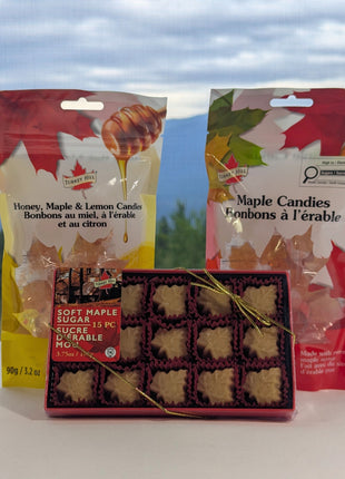 Canadian maple treat sampler displayed in front of a scenic mountain and forest landscape, with soft maple sugar candies, traditional maple candies, and honey, maple and lemon candies.  The outdoor Canadian setting adds a natural regional feel while keeping all three maple treats visible as a coordinated sampler.