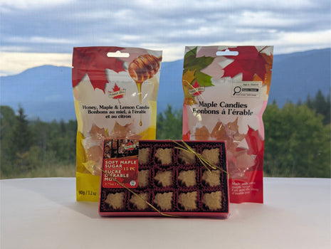 Canadian maple treat sampler displayed in front of a scenic mountain and forest landscape, with soft maple sugar candies, traditional maple candies, and honey, maple and lemon candies.  The outdoor Canadian setting adds a natural regional feel while keeping all three maple treats visible as a coordinated sampler.