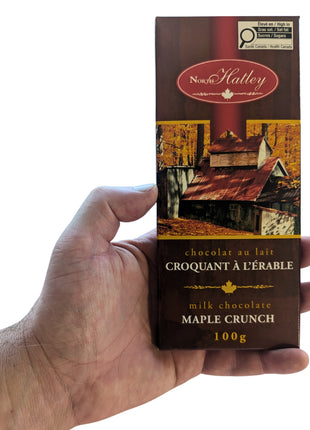 A 100 g Canadian Milk Chocolate Maple Crunch bar held in one hand to show the size and scale of the package. A Canadian maple chocolate treat made with milk chocolate and maple sugar.