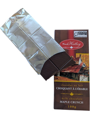 Partially unwrapped Canadian Milk Chocolate Maple Crunch bar showing the segmented chocolate squares beside its package. This 100 g Canadian maple treat combines milk chocolate with maple sugar.