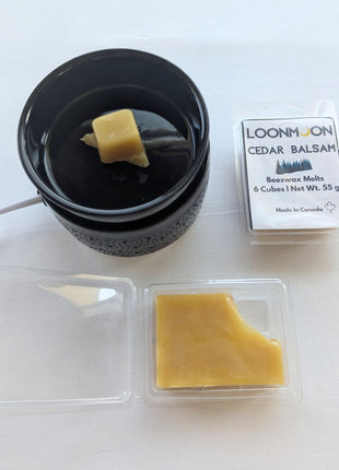 LOONMOON Cedar Balsam beeswax melts displayed beside a black wax warmer with one wax cube in the dish and an open clamshell revealing the natural wax inside.  The image combines packaging, wax texture, and a simple in-use setup to show how the cedar balsam beeswax melts look during use.
