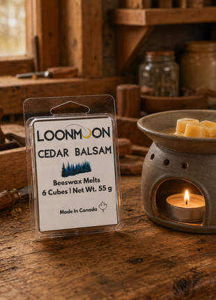 LOONMOON Cedar Balsam beeswax wax melts beside a glowing ceramic warmer on a rustic woodshop bench.