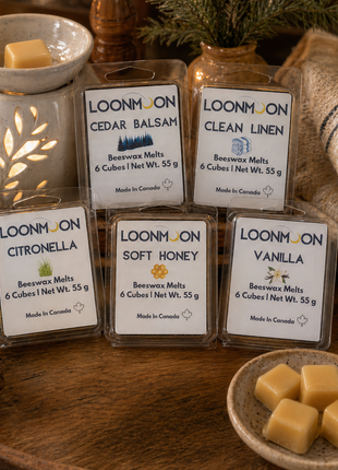 LOONMOON beeswax wax melts in five scents beside a glowing ceramic warmer and beeswax cubes on a rustic wooden table.