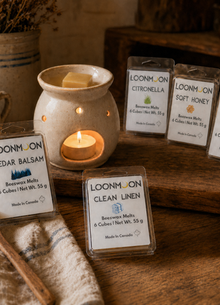 LOONMOON beeswax wax melts in five scents displayed with a glowing ceramic wax warmer on a rustic wooden table.