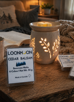 LOONMOON Cedar Balsam beeswax wax melts beside a glowing ceramic warmer in a cozy reading nook.