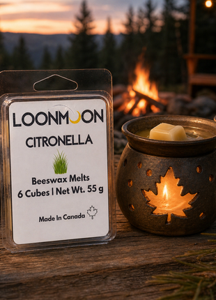 LOONMOON Citronella beeswax wax melts beside a glowing maple leaf warmer on a rustic outdoor picnic table near a campfire.
