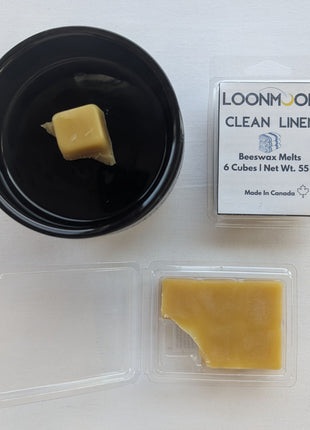 LOONMOON Clean Linen beeswax melts displayed with a black wax warmer, one wax cube in the warmer dish, and an open clamshell showing the wax inside.  This image presents the Clean Linen scent in a practical lifestyle-style setup while still clearly showing the product and packaging.