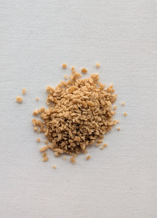 A close-up of a small pile of coarse maple sugar crystals on a clean white background, showing the natural golden-brown colour, irregular granule size, dry crystalline texture and larger pieces that distinguish this coarse maple sugar from a finely ground variety.