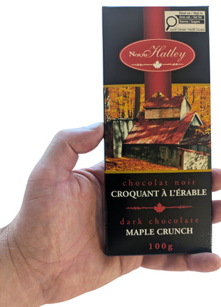 A 100 g Dark Chocolate Maple Crunch bar held in one hand to show the size and scale of the package. Made in Canada, this dark chocolate maple treat combines chocolate with Canadian maple sugar.