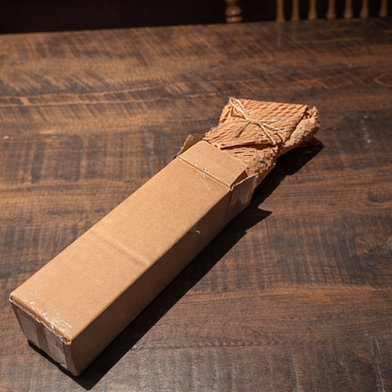 Six beeswax taper candles wrapped in honeycomb paper and placed in a kraft cardboard shipping box.