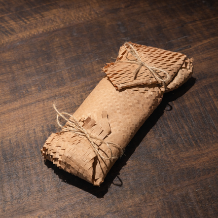 Finished package of six beeswax taper candles wrapped in honeycomb kraft paper with twine ties on a wooden table.