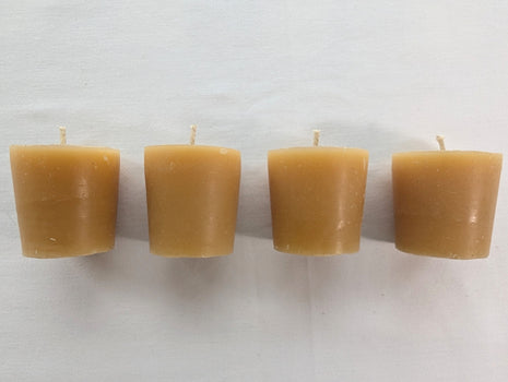 Four unwrapped beeswax votive refill candles are lined up against a clean white background.  The image clearly shows their compact tapered shape, warm natural wax colour, cotton wicks, and slight handmade variation.