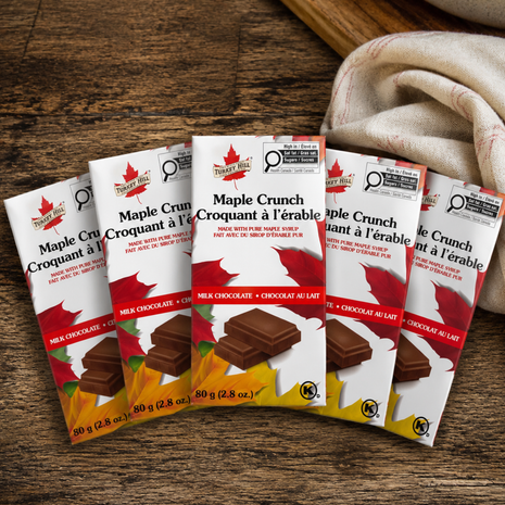 Five Turkey Hill Maple Crunch milk chocolate bars arranged fan-style on a rustic wooden table, showing 80g Canadian maple chocolate packaging for a shareable 5-pack bundle.