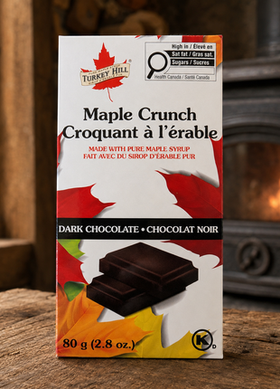 Maple Crunch dark chocolate bar on a rustic wooden table with a wood stove in the background.