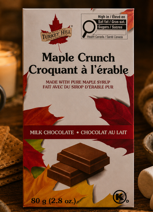 Turkey Hill Maple Crunch Belgian milk chocolate bar surrounded by graham crackers, marshmallows, and chocolate pieces beside a warm candlelit fireplace.