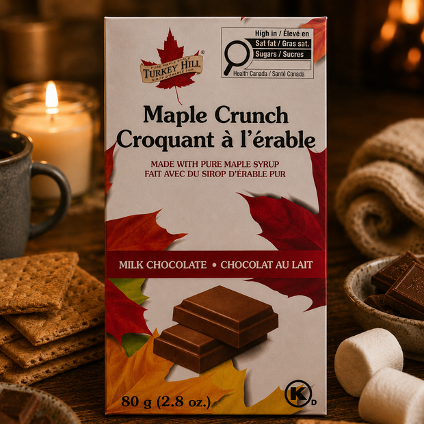 Turkey Hill Maple Crunch Belgian milk chocolate bar surrounded by graham crackers, marshmallows, and chocolate pieces beside a warm candlelit fireplace.
