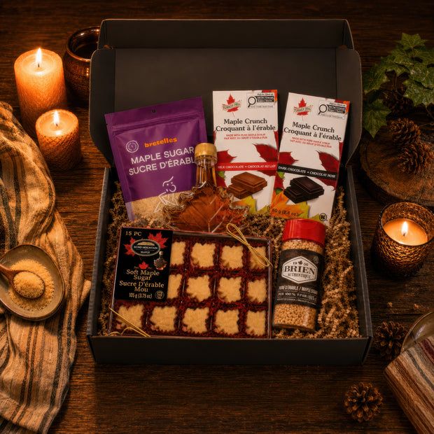 Premium Canadian maple gift box with maple syrup, maple sugar, soft maple candies, and milk and dark maple crunch chocolate bars, arranged in a black gift box on a rustic candlelit table.