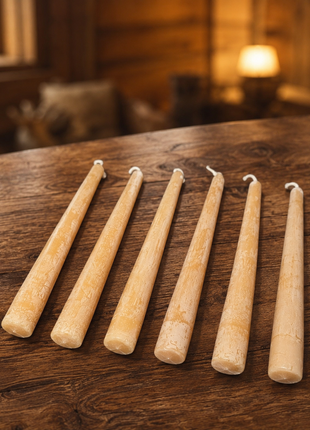 Set of 6 handmade 100% pure beeswax taper candles on a rustic wooden table with warm cabin background