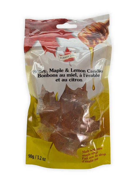 A front view of a 90 g resealable package of Honey, Maple & Lemon Candies photographed on a clean white background.  The bilingual English and French label, honey dipper and lemon artwork, colourful maple-leaf design, and individually wrapped amber maple-leaf hard candies are clearly visible through the transparent package window.