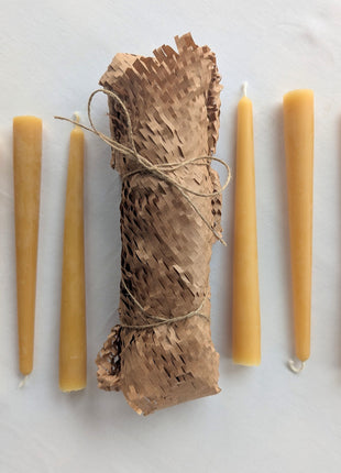 Six natural beeswax taper candles arranged around their honeycomb-paper-wrapped bundle on a soft white background.  This complete six-candle set shows the warm golden beeswax colour, natural surface variation, cotton wicks and low-plastic kraft-paper presentation used for the LOONMOON taper candle package.