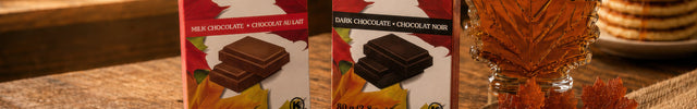Canadian maple treats collection with Maple Crunch Belgian milk and dark chocolate bars, maple leaf syrup bottle, soft maple sugar candies, and amber maple candies on a rustic wooden table.